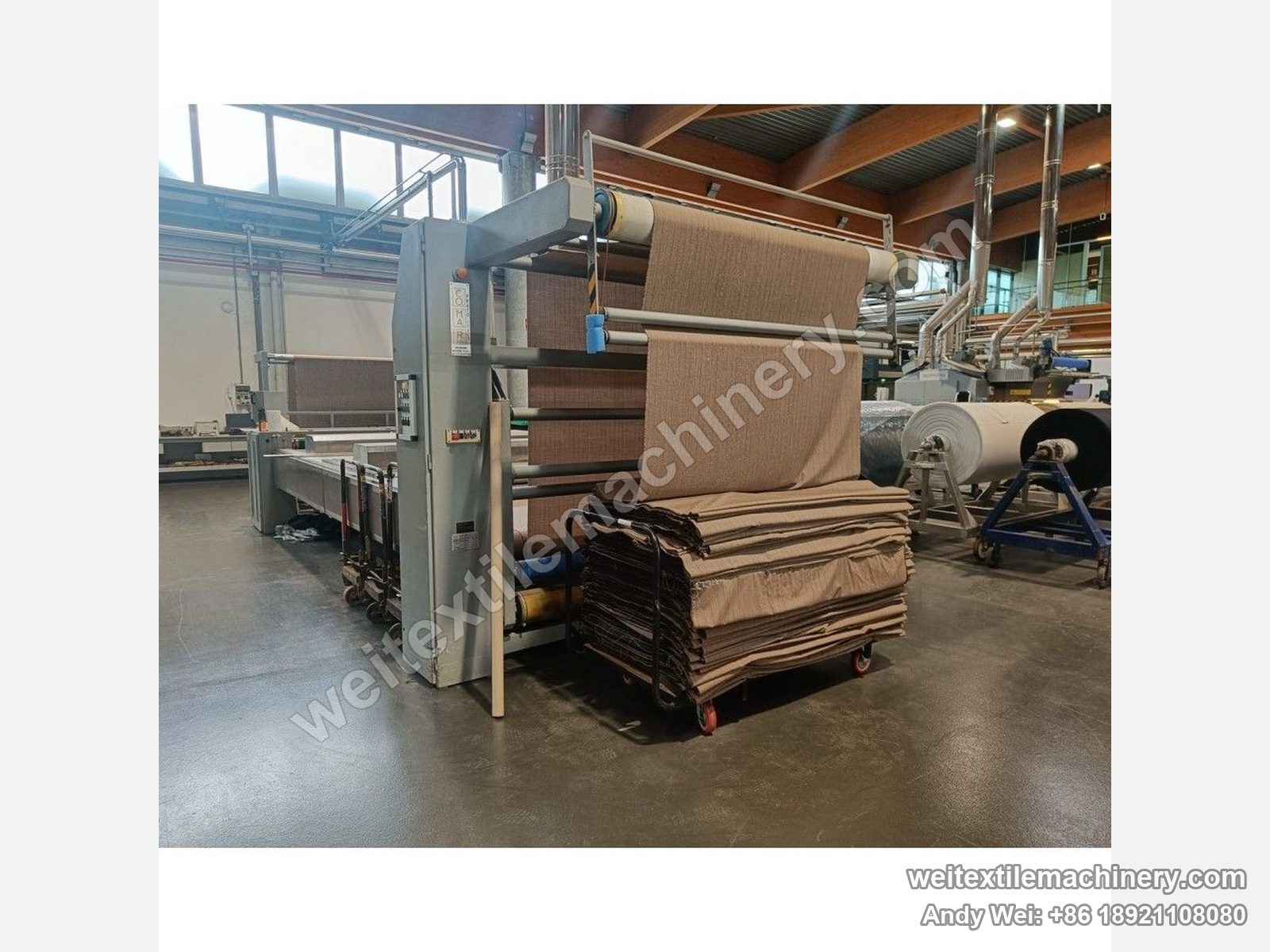Used CoMaR VAPORAMA belt-type steaming-shrinking machine, delivery end with the COMAR badge, fabric plaited down into a trolley
