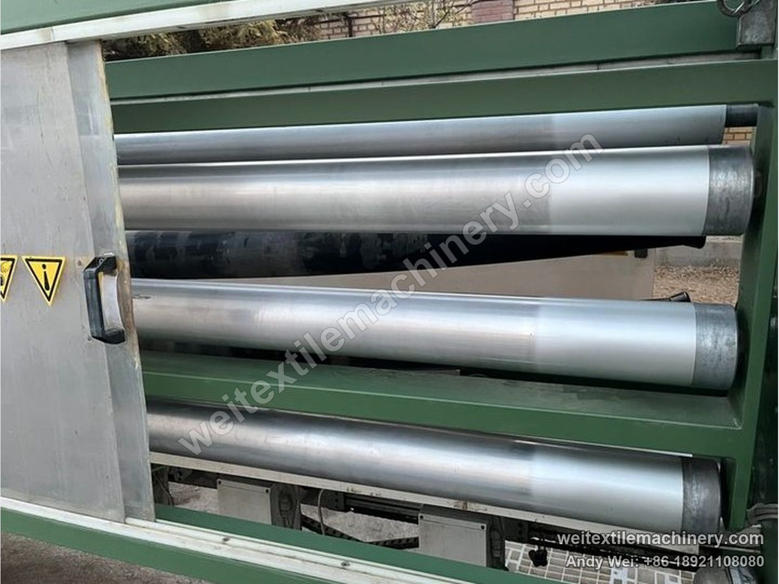 Used Corino photoelectric weft straightener, roll stack close-up with stainless straight and bowed rolls inside the green frame and warning labels