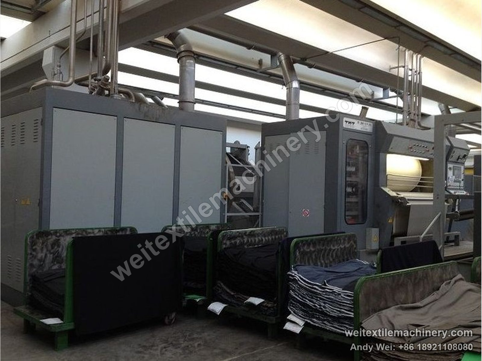 Used TMT PF2000-1593 kier decatizing machine, full view with dark grey body, inspection door and panel, fabric carts in front and overhead ducting