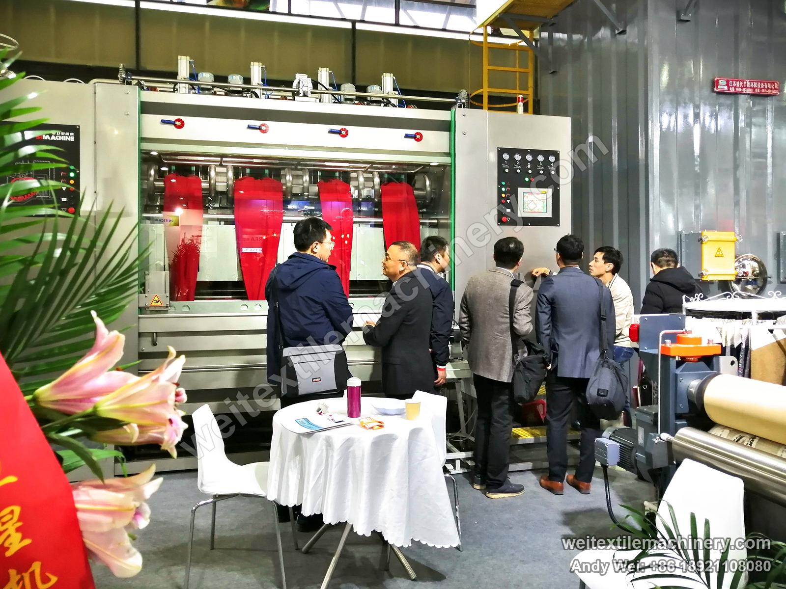 Visitors gathered at a four-channel scouring and milling machine on the 2019 stand, red fabric in each channel