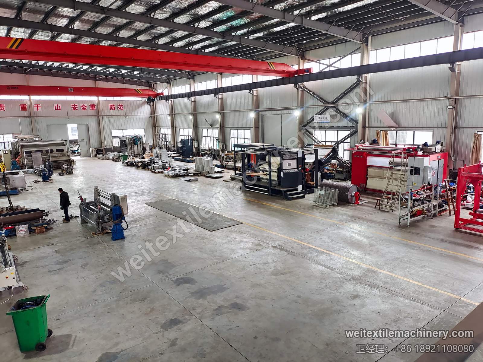 千立右侧车间，开阔地坪上摆放多台设备与部件，上方为红色行车，操作人员在场